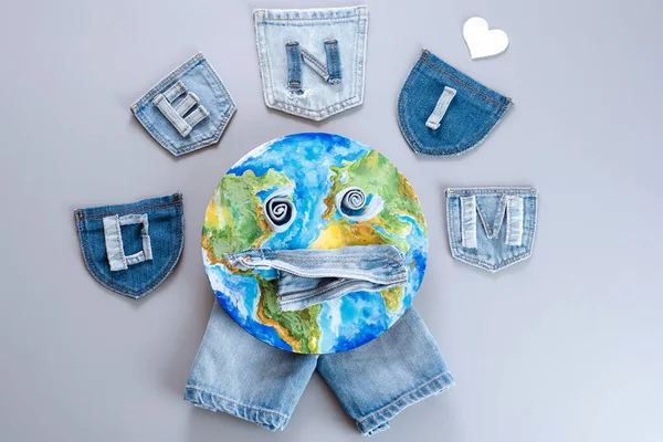 Sad Earth planet from of denim pieces. Isolated on gray background, top view. Fabric and clothing denim sustainability. Save ecology. High quality photo