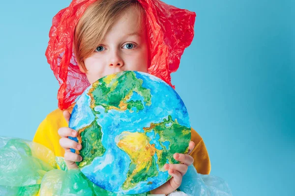 Creative concept International Plastic Bag Free Day. Portrait of a child dressing in plastic bags holding a painted planet Earth in front of his face. Save nature. Pollution and addiction to plastic. High quality photo
