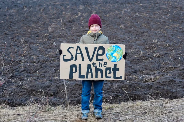 A boy holding a cardboard sign save the planet on the background of arable land. Farmland preservation concept. High quality photo