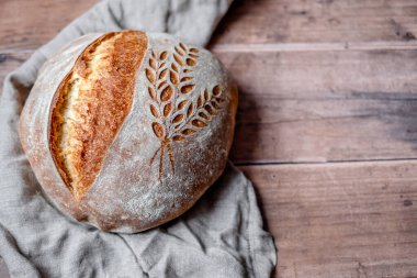 Homemade organic bread with a pattern ears of wheat. Scoring bread wheat bread on a wooden table. Artisan sourdough bread recipe. Healthy eating. 