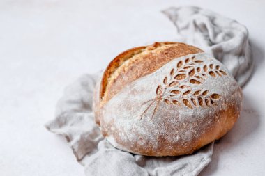 Rustic Italian Bread with Lievito Madre on a napkin on a white table. Scoring an ears and wheat pattern. Cooking of healthy bread from alternative flours. Fermented food. High quality photo