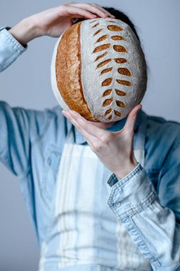 Sourdough Bread Scoring pattern. A woman covering her face with freshly baked bread. The edible art of sourdough. High quality photo