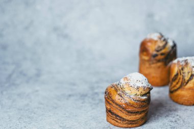 Easter background. Cruffin buns on sprinkled with powdered sugar, filling with poppy seeds on a gray background. Healthy holiday baking. High quality photo