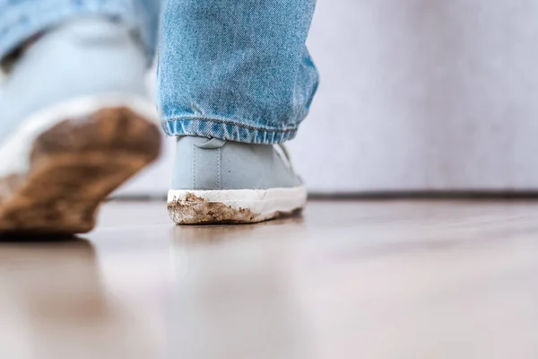 An unrecognizable child walking indoors of the apartment in dirty sneakers and leaving stains in the floor. Mud footprint on floor. Daily life dirty stain. High quality photo