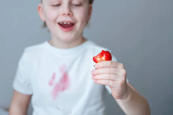 子供の手はイチゴのスライスを保持しています 白いTシャツの前に汚れたピンクの汚れ 日常生活の汚れの概念 高品質の写真 — ストック写真