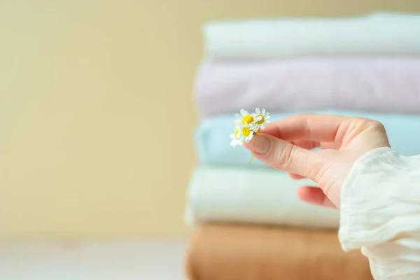 A female is holding daisies on the background of a stack of summer clothes. Change of wardrobe season. Summer slow fashion concept. High quality photo