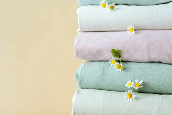 Stack of clothes with daisies on the beige background. Change of wardrobe season. Natural sustainable clothing . High quality photo