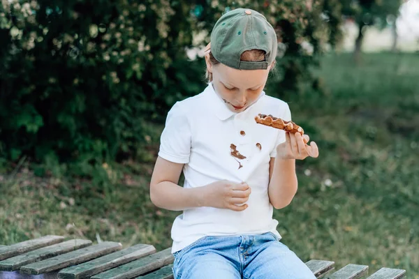 stock image A child showing a chocolate stains on his clothes sitting on a wooden bench in the park. outdoors. The concept of cleaning stains on clothes. High quality photo