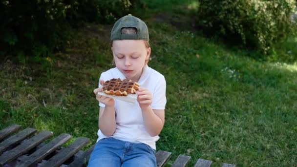 一个小孩坐在公园的木制长椅上吃巧克力蛋糕 高质量的4K镜头 — 图库视频影像