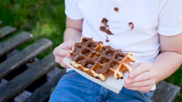 一个小孩用粘巧克力手吃比利时华夫饼的特写镜头 衣服上都是肮脏的巧克力脏衣服 — 图库视频影像
