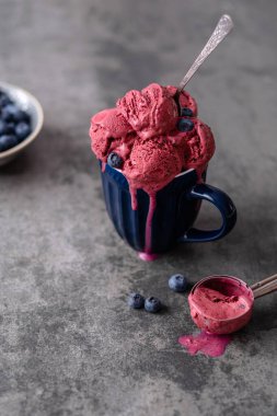 Ev yapımı vejetaryen dondurma kepçeleri, çimentoda kaşıkla servis edilen mavi bardakta eriyor. Sağlıklı dondurulmuş tatlı. Vegan gıda konsepti. Yaz ve Tatlı menü. Yan görünüş. Yüksek kalite fotoğraf