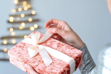 Kadın eli, Noel ağacının arka planında pembe hediye kutusunu açıyor. Noel için bayram hediyesi. Yüksek kalite fotoğraf