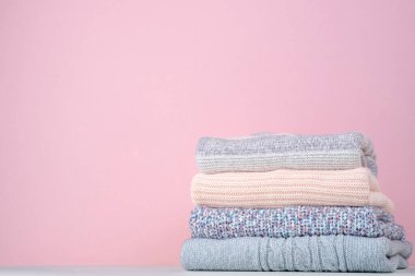 Pembe arka planda kışın örülmüş kazak yığını. Mevsim değişimi. Bilinçli tüketim. Çevresel dostluk ve sürdürülebilir moda. Metin için boşluk. Yüksek kalite fotoğraf
