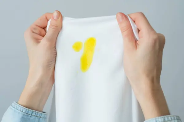 Unrecognizable woman holding white clothes with a yellow stain. Spoiled clothes food or a pet. daily life stain concept. top view. High quality photo