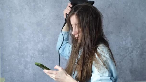 Девушка Сушит Влажные Волосы Феном Набирает Сообщение Телефону Сером Фоне — стоковое видео
