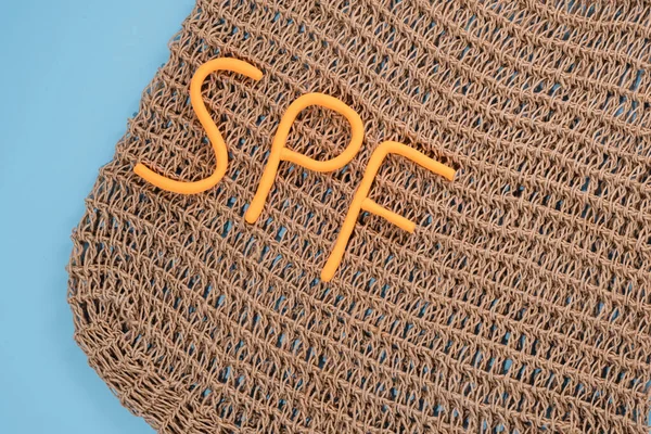Creative composition wicker bag with the word spf on a blue background. Summer mood. Daily skin protection. Flat lay. High quality photo