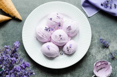 Beyaz bir tabakta lavantalı kremalı dondurma, lavanta çiçekleriyle süslenmiş. Üst Manzara. Sağlıklı dondurulmuş tatlı. Yüksek kalite fotoğraf