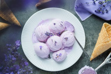 Beyaz bir tabakta lavantalı kremalı dondurma, lavanta çiçekleriyle süslenmiş. Üst Manzara. Sağlıklı dondurulmuş tatlı. Yüksek kalite fotoğraf