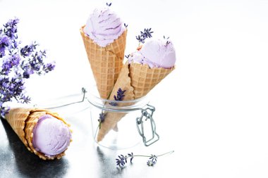 Lavanta çiçekleriyle süslenmiş cam bir kavanozda waffle külahında iki kremalı lavantalı dondurma. Metin için boşluk. Sağlıklı dondurulmuş tatlı. Yüksek kalite fotoğraf