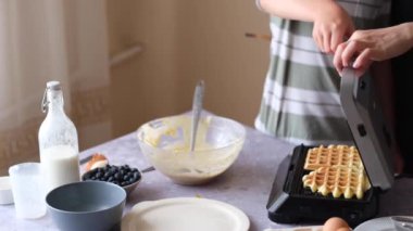 Bir kadın ve oğlu waffle makinesi pişiriyor. Kabarık ev yapımı Belçika waffle 'ı. Yemek pişirme süreci. Sağlıklı kahvaltı. Vejetaryen ve sağlıklı waffle. 4k video. Yüksek kalite 4k görüntü