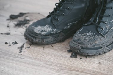 Muddy black boots and muddy footprints on a wooden floor, leaving a major mud cakes. Concept of cleaning mud in wet weather messes. top view . High quality photo clipart