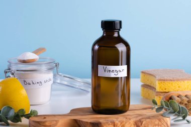 İçinde limon, kabartma tozu, mavi arka planda temizlik süngeri gibi temizlik malzemeleri olan koyu renkli bir sirke şişesi. Lekeleri çıkarmak için doğal ürünleri kullanarak DIY temizlik yöntemi. Yüksek kalite fotoğraf