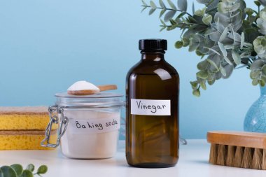 İçinde limon, kabartma tozu, mavi arka planda temizlik süngeri gibi temizlik malzemeleri olan koyu renkli bir sirke şişesi. Lekeleri çıkarmak için doğal ürünleri kullanarak DIY temizlik yöntemi. Yüksek kalite fotoğraf