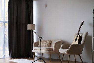 Oturma odasında iki yumuşak koltuk, bir gitar ve bir lamba bulunur. Doğal ışık perdelerin arasından süzülerek sıcak ve davetkar bir atmosfer yaratır. Yüksek kalite fotoğraf