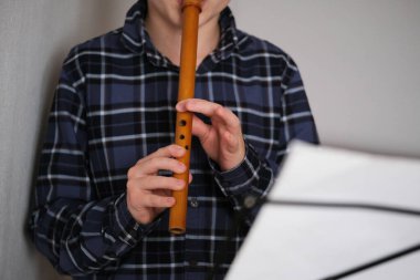 A child playing a wooden reed pipe on a gray background, music class in modern studio setting while focusing on his performance. High quality photo clipart