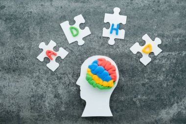 Renkli malzemelerden yapılan bir beyin modeli, bu durumun farkındalığını ve anlayışını vurgulayan ADHD etiketli yapboz parçalarıyla çevrili beyaz bir kafa siluetine dayanır. Yüksek kalite fotoğraf