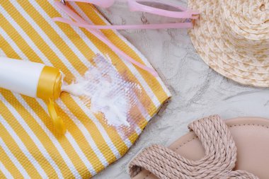 Güneşli bir günde plaj havlusuna, sandaletlerin yanına ve hasır şapkaya güneş kremi dökülür. Kıyafetlerdeki günlük kozmetik lekeleri. Üst Manzara. Yüksek kalite fotoğraf