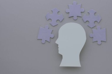 Bir kafa silueti gri arka planda bulmaca parçalarıyla çevrilidir, basit, minimalist bir tasarımla yaratıcı düşünme ve problem çözme kavramını temsil eder. Yüksek kalite fotoğraf