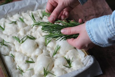 Unrecognizable person hands sprinkle rosemary on fluffy bread dough as it rises the preparation stage for baking in a cozy kitchen setting. Italian flat bread. High quality photo