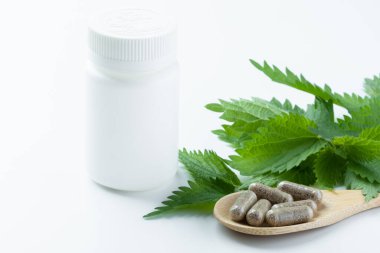 Isırgan otu yaprakları minimalist bir yüzeyde sade beyaz bir takviye şişesinin etrafına dizilir ve temiz bir ortamda doğal sağlık ve ilaçlara odaklanır. Yüksek kalite fotoğraf