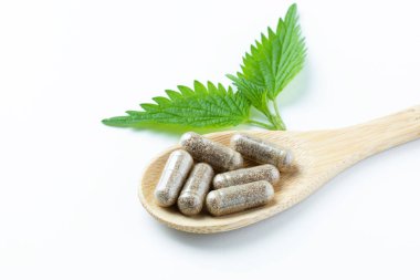 Tahta kaşıkta bitkisel takviyeler ve beyaz arka planda ısırgan otu. Alternatif tıp, sağlıklı ve refah temalı konsept. Beslenme takviyesi kavramı. Yüksek kalite fotoğraf