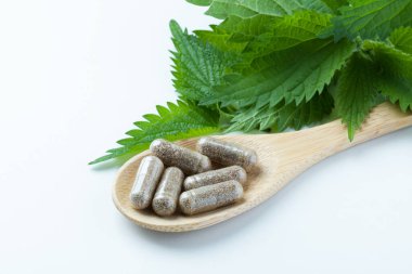 Tahta kaşıkta bitkisel takviyeler ve beyaz arka planda ısırgan otu. Alternatif tıp, sağlıklı ve refah temalı konsept. Beslenme takviyesi kavramı. Yüksek kalite fotoğraf