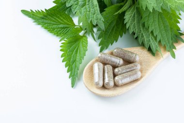 Tahta kaşıkta bitkisel takviyeler ve beyaz arka planda ısırgan otu. Alternatif tıp, sağlıklı ve refah temalı konsept. Beslenme takviyesi kavramı. Üst Manzara. Yüksek kalite fotoğraf