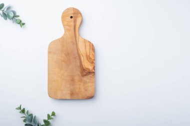 Beyaz bir yüzeye yerleştirilmiş ahşap bir kesme tahtası, etrafa yayılmış canlı okaliptüs yapraklarıyla süslenmiş, mutfak ortamında taze ve doğal bir görünüm yaratıyor. Üst Manzara. Yüksek kalite fotoğraf