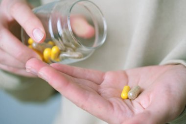Bir insan eline cam kaplardan rengarenk diyet kapsülleri dökerek ağrı kesici, ilaç, vitamin ya da antibiyotik alır. Sağlık kavramı. 