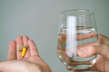 Ellerinizi iki kapsül ve bir bardak suyla kapatın, sabahları daha iyi olmak için beslenme takviyeleri almanın yaygın bir uygulama olduğunu göstermektedir. Sağlık konsepti. Yüksek kalite fotoğraf