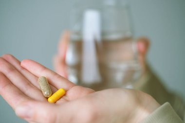 Ellerinizi iki kapsül ve bir bardak suyla kapatın, sabahları daha iyi olmak için beslenme takviyeleri almanın yaygın bir uygulama olduğunu göstermektedir. Sağlık konsepti. Yüksek kalite fotoğraf