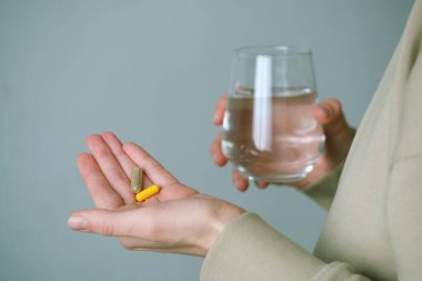 Ellerinizi iki kapsül ve bir bardak suyla kapatın, sabahları daha iyi olmak için beslenme takviyeleri almanın yaygın bir uygulama olduğunu göstermektedir. Sağlık konsepti. Yüksek kalite fotoğraf