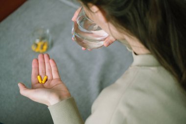 Ellerinizi iki sarı kapsül ve bir bardak suyla kapayın, bu da sabahları daha iyi olmak için beslenme takviyeleri almanın yaygın bir uygulama olduğunu gösteriyor. Sağlık konsepti. Üst Manzara. Yüksek kalite fotoğraf