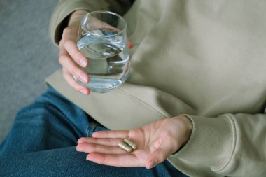 Ellerinizi iki bitkisel kapsül ve bir bardak suyla kapayın, bu da sabahları daha iyi olmak için beslenme takviyeleri almanın yaygın bir uygulama olduğunu gösteriyor. Sağlık konsepti. Üst Manzara. Yüksek kalite fotoğraf