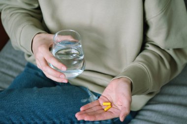 İki sarı kapsül ve bir bardak suyla ellerini kapat. Alternatif tıp, sağlıklı ve refah temalı konsept. Sağlık konsepti. Üst Manzara. Yüksek kalite fotoğraf