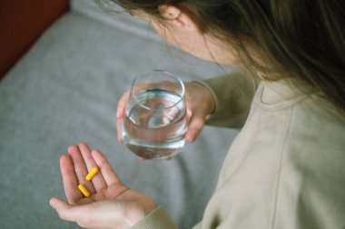 İki sarı kapsül ve bir bardak suyla ellerini kapat. Alternatif tıp, sağlıklı ve refah temalı konsept. Sağlık konsepti. Üst Manzara. Yüksek kalite fotoğraf