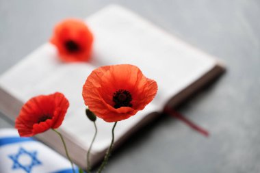 Açık bir kitabın yanına koyulmuş parlak turuncu gelincikler. İsrail bayrağı, hatıra ve umudun sembolü. Savaş anıtı tatili. Yahudi Anma Günleri. Yüksek kalite fotoğraf