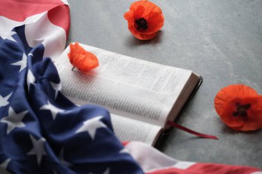 Yakındaki Amerikan bayrağını süsleyen parlak gelincik çiçekleri ve gri arka planda açık bir İncil. Anma Günü, Gaziler Günü ya da gri bir arkaplanda anma günü. Yüksek kalite fotoğraf