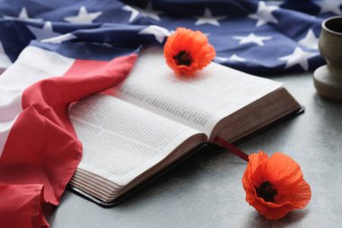 Amerikan bayrağı parlak gelincik çiçeklerini gri arka planda açık bir İncil 'de süsledi.. 