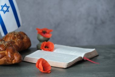 Açık bir kitabın yanına konmuş parlak turuncu gelincikler geleneksel challah ekmeği, İsrail bayrağı bir hatıra ve umut sembolü. Savaş anıtı tatili. Yahudi Anma Günleri. Yüksek kalite fotoğraf